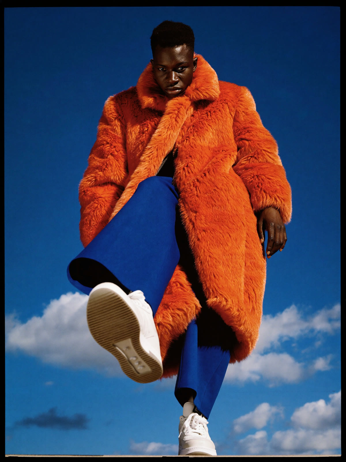AI campaign: orange faux-fur coat and cobalt trousers against the sky